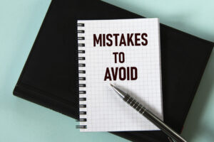MISTAKES TO AVOID - words in a white notebook against the background of a black notebook with a pen. 